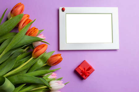 Empty picture frame next to a bouquet of tulips and a red gift boxの写真素材