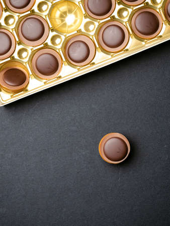 Chocolate candies in a gold box over black background, top view, place for textの写真素材