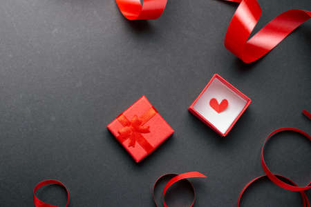 Red gift box with a red heart shape over black background. Concept minimalist greeting cardの写真素材