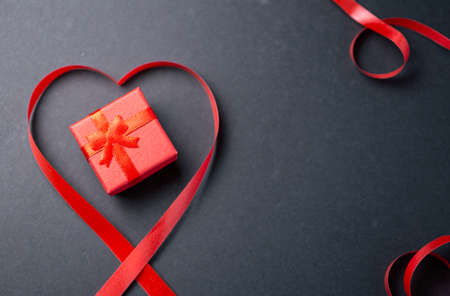 Red gift box with heart made from red gift bow over black backgroundの写真素材
