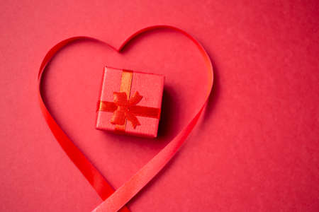 Red gift box with heart made from red gift bow over red background. Romantic greating card.の写真素材