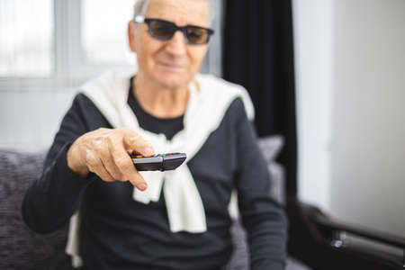 Senior man with 3D glasses and TV remote control in handの写真素材