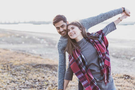 Happy young joyful couple having beach fun moments laughing together in autumn season with place for...