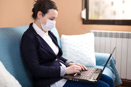 Business woman with medical mask working from home, concept of home working during quarantine periodの写真素材