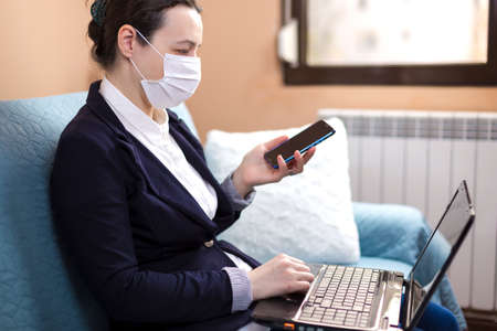 Woman with medical mask working from home, concept of home working during quarantine periodの写真素材