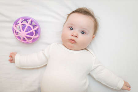 Cute Baby Girl Infant Stand on Back in Crib near a Sensory Toyの写真素材