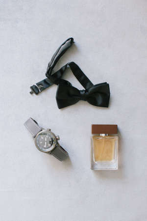 Groom accessories. Wristwatch, bow tie and perfume. On the gray background.