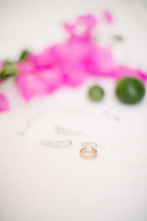 Wedding rings and jewelry. On a white background and pink bougainvillea leaves and lime.の写真素材