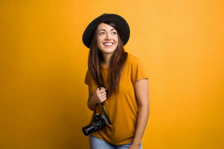 Pretty lady smiling holding a photo camera with her hands. Adorable little girl in orange t-shirt on colorful backgroundの写真素材
