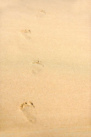 Human footprints on the beach sand leading away from the viewer
