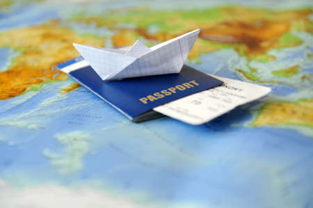 Paper boat, passport on a background map of the world. Traveling concept