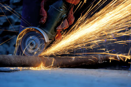 Worker cutting metal with grinder. Sparks while grinding iron