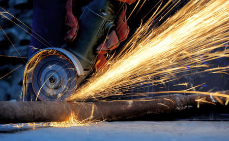 Worker cutting metal with grinder. Sparks while grinding iron