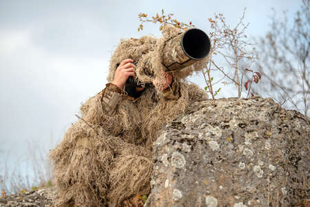 Camouflage wildlife photographer in the ghillie suit working in the wild