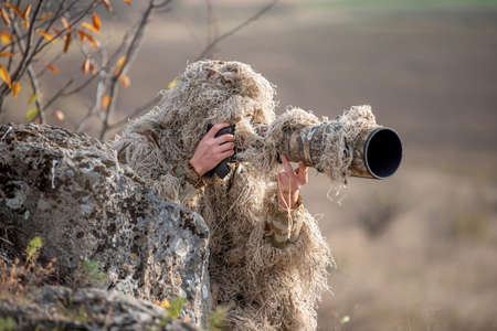 Camouflage wildlife photographer in the ghillie suit working in the wild