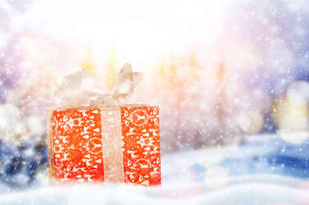 Decorative red gift box with a large bow standing in fresh snow on winter backgroundの写真素材