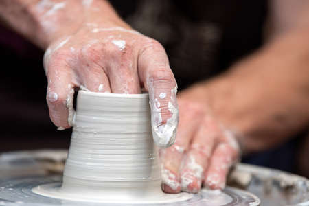 Hands of the potter. The potter makes pottery dishes on potter's wheel. The sculptor in workshop...