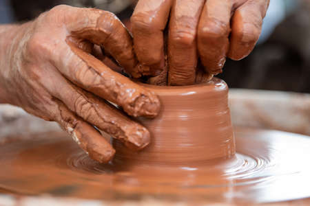Hands of the potter. The potter makes pottery dishes on potter's wheel. The sculptor in workshop...