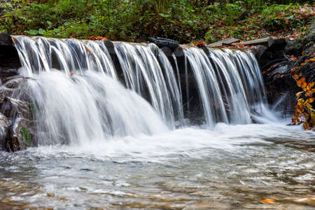 Autumn  waterfall with yellow trees foliage and rocks in forest mountain