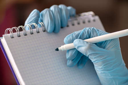 Female hand in a medical glove holds a tablet for writing and a pen. Medicine concept