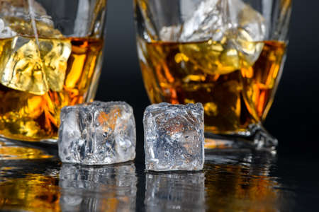 Glass of whiskey or other alcohol with cube ice on black backgroundの写真素材