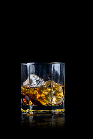 Glass of whiskey or other alcohol with cube ice on black background