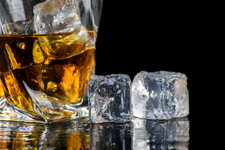 Glass of whiskey or other alcohol with cube ice on black backgroundの写真素材
