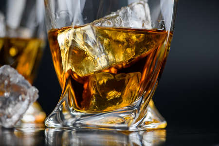 Glass of whiskey or other alcohol with cube ice on black backgroundの写真素材