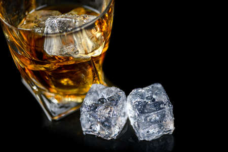 Glass of whiskey or other alcohol with cube ice on black backgroundの写真素材