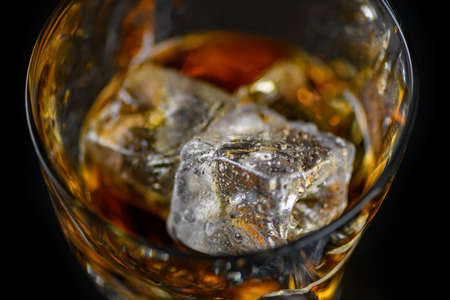 Glass of whiskey or other alcohol with cube ice on black background