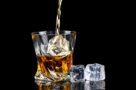 Glass of whiskey or other alcohol with cube ice on black backgroundの写真素材