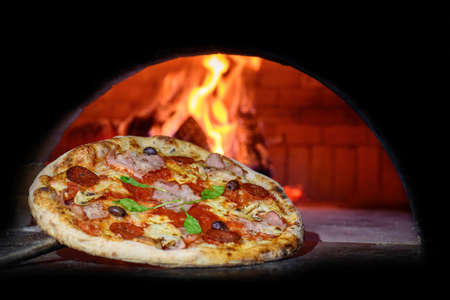 Close Delicious Italian pizza in a shovel putting in wood burning ovenの写真素材