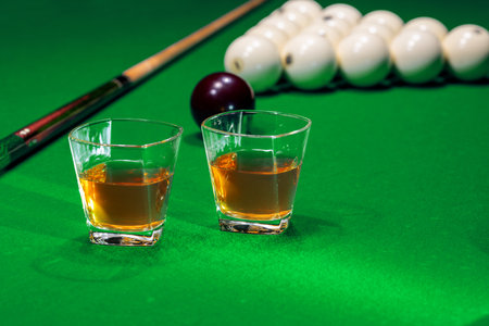 Two glass of whiskey on billiard table with cue and billiard balls in backgroundの写真素材