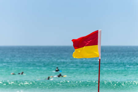 Red and yellow flag marking the limit of the safe swimming area on a beach under a blue summer skyの写真素材