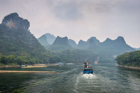 Xingping, China - October 20, 2013: A tourist boats travels the magnificent scenic route along the Li river from Guilin to Yangshou in cloudy weather.のeditorial素材