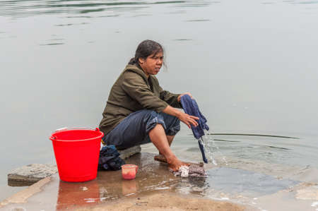 Yangshuo, China - October 20, 2013: Village in China, in countryside, rural Asian farm. Chinese peasant woman washing his clothes in water river near Yangshuo, China.のeditorial素材