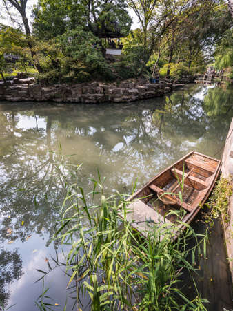 Suzhou, China - October 23,2016: Small Chinese wooden boat with reflected trees in the Humble Administrator's Garden, Suzhou, China.のeditorial素材