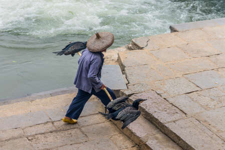 Cormorant fisherman goes to his ancient bamboo raft on the Li River in Yangshuo, Guangxi, China.の写真素材