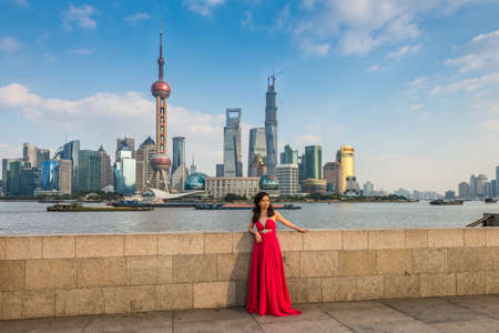 Shanghai, China - October 26, 2013: Chinese woman in a long red dress at the Bund. It is a waterfront area, central Shanghai, which runs along the western bank of Huangpu River, facing Pudong skyscrapers, Shanghai, Chinaのeditorial素材