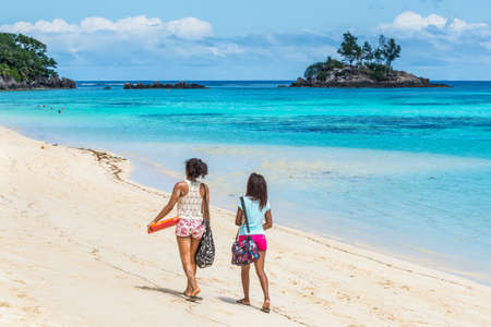 Anse Royale, Mahe Island, Seychelles - December 15,2015: Girls walking in the sand in Spectacular Anse Royale beach and in the background some people enjoying the Anse Royale Beach, Mahe Island, Seychelles.のeditorial素材