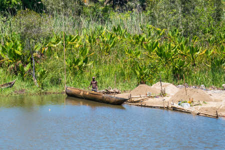 Ivoloina, Madagascar - December 22, 2015: Malagasy countryside man from the village unload sand from traditional handmade dugout wooden boats near the city of Toamasina (Tamatave), Madagascar, East Africa. Everyday life on the river.のeditorial素材