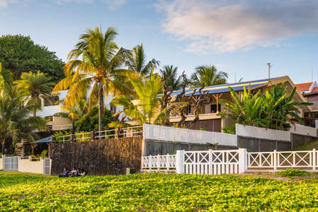 Blue Bay, Mauritius - December 27, 2015: People are sitting on the grass near the wall of the house and palm trees on tropical Blue Bay beach at sunset, Mauritius Island.のeditorial素材