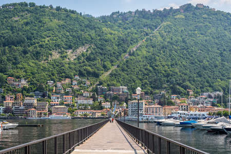 Como, Italy - May 27, 2016: People walk on the Diga Piero Foranea Caldirola pier at Como lake in Como town Lombardy region of Italy Europe. Cable car Como - Brunate on the background.のeditorial素材