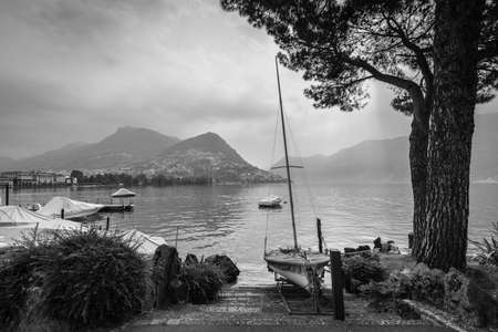 Boats and trees on Lake Lugano, mountain Monte Bre in the background. Black and white photography.の写真素材