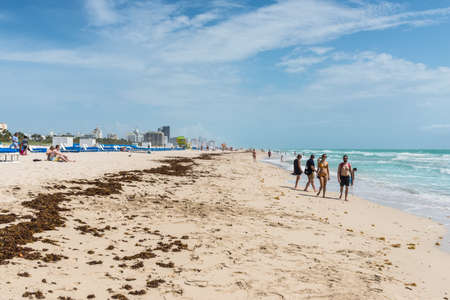 Miami, FL, USA - April 19, 2019: People on beach enjoying sun in South Beach Miami, situated just across the famous Art Deco District Strip in Miami, Florida, United States of America. Seaweed on the sand.のeditorial素材