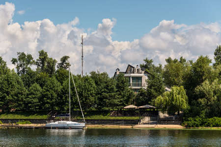 Kyiv, Ukraine - July 13, 2019: A sailing yacht is moored to the shore and a building on the banks of the Dnipro River in Kyiv, Ukraine. Beautiful summer landscape view on Trukhaniv Island.のeditorial素材