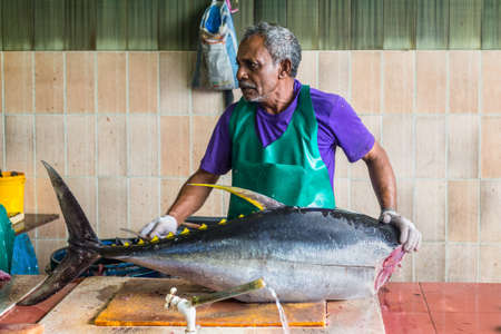 Male, Maldives - November 16, 2017: Man prepares fresh fish (big tuna) for sale at the Fish Market in the city and island of Male, capital of Maldives.のeditorial素材