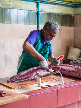 Male, Maldives - November 16, 2017: Man cutting big tuna fish for sale at the Fish Market in the city and island of Male, capital of Maldives.のeditorial素材