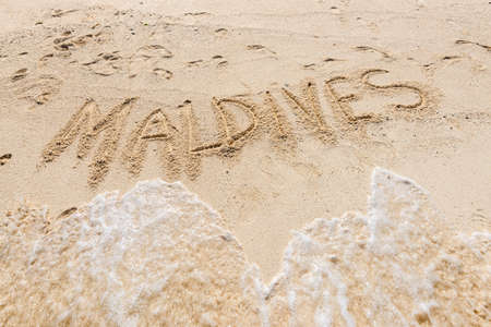 Handwriting word "Maldives" on maldivian beach drawn on sand and sea wave, travel destinations concept cardの写真素材