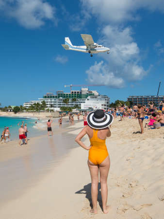 Maho beach, Saint Martin - December 17, 2018: A airplane approaches Princess Juliana airport above onlooking spectators. Woman on cruise ship vacation travel relaxing in famous touristic destination.のeditorial素材